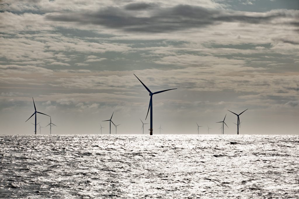 An offshore wind turbine with the sun shining off the sea in front