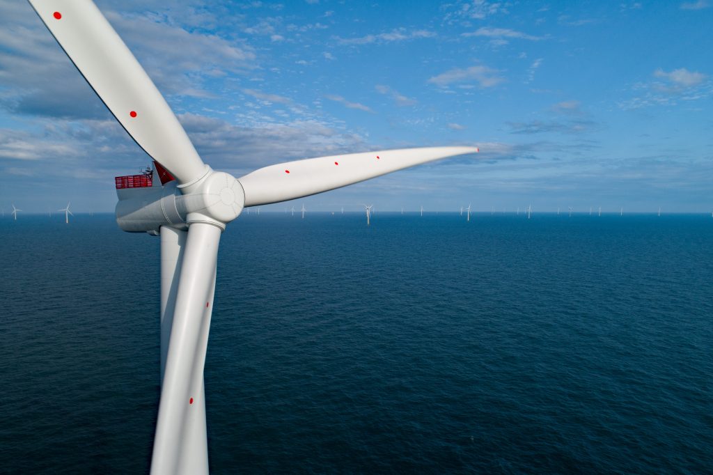 A close up view of an offshore wind turbine with a wind farm in the background surrounded by sea